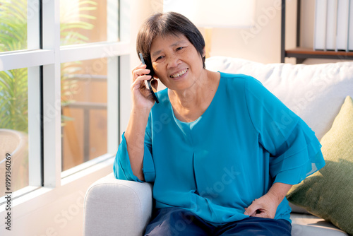 Senior asian woman telephone smiling and relax sitting on sofa in living room at home, cheerful elderly woman talking with smart phone sitting on couch in home, lifestyle and communication.