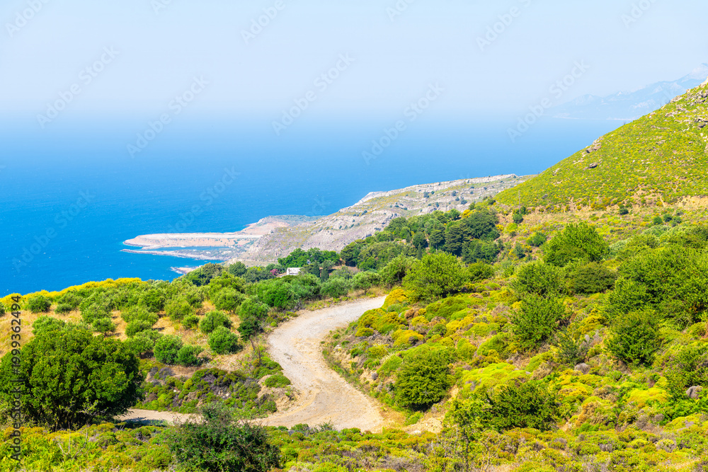 Fototapeta premium Perdiki village at Ikaria island northern shore coast, Greece with Faros airport runway, farm garden building by street road