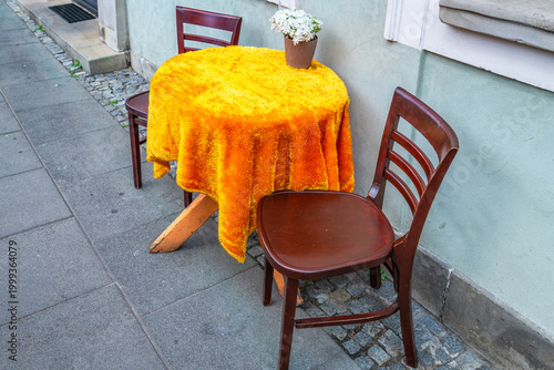 Empty wooden table two chairs outside restaurant cafe on sidewalk street, white flowers in flowerpot potted plant setting in Warsaw Poland