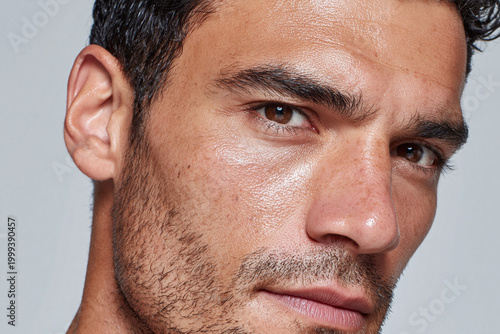 Close up male face hydrated cheek area reflecting skin texture brown eye stubble intense gaze natural light smooth complexion warm tone