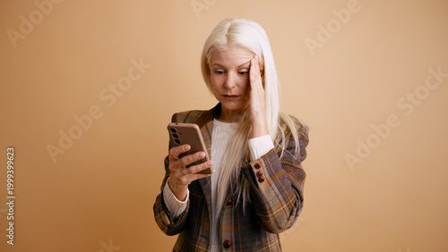 Fotografie Senior woman in plaid blazer receiving bad news on her mobile phone, experiencin