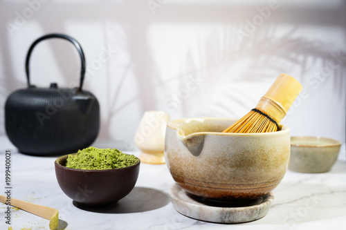 Close-up of matcha green tea powder in a bowl with bamboo spoon and whisk.