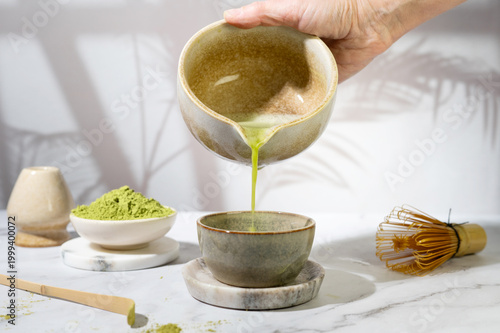Woman pouring smooth matcha tea from a bowl into a cup.