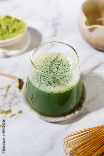 Glass of matcha green tea with creamy foam, styled with bamboo whisk and spoon.