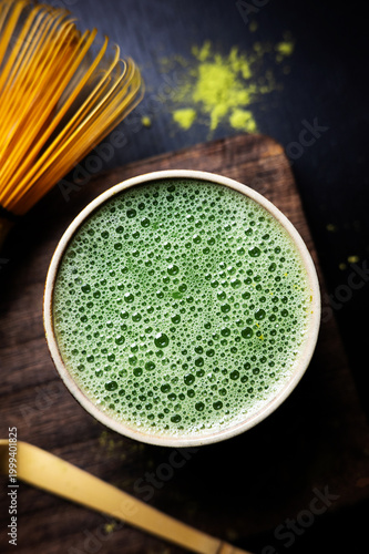 Close-up of matcha tea foam in a cup with bamboo whisk and spoon.