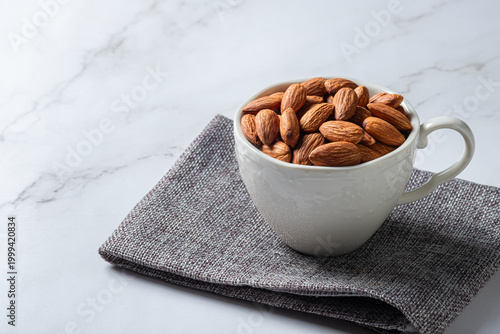 Roasted almonds in a white cup on marble background with copy space.