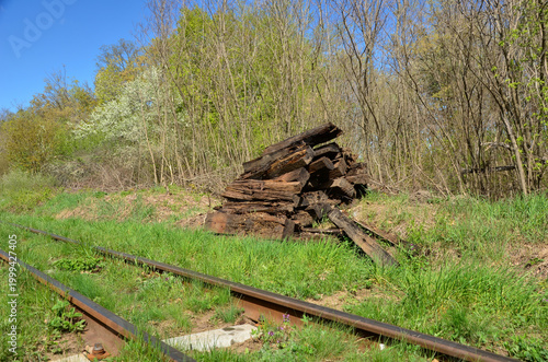 Pile of old wooden railway sleepers on green grass near tracks in a spring forest. 
