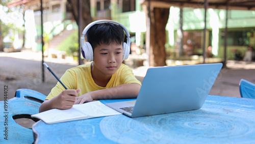 Focused Asian Boy Student Using Laptop and Headphones for E-learning in Outdoor Classroom