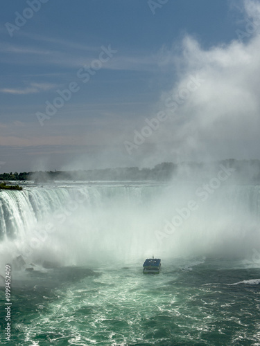 A tour boat loaded with tourists in blue ponchos cruises towards the mist at the base of the Horseshoe Falls in Niagara Falls, Ontario, Canada.