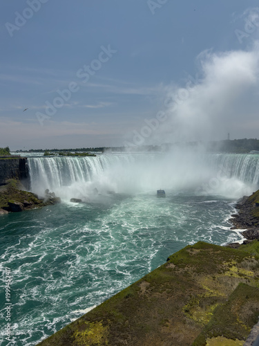 A tour boat loaded with tourists in blue ponchos cruises towards the mist at the base of the Horseshoe Falls in Niagara Falls, Ontario, Canada.