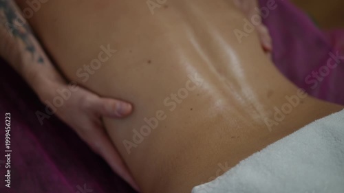 Close-up of a therapist's hands performing a relaxing back massage on a client lying on a massage table. Wellness and body care concept