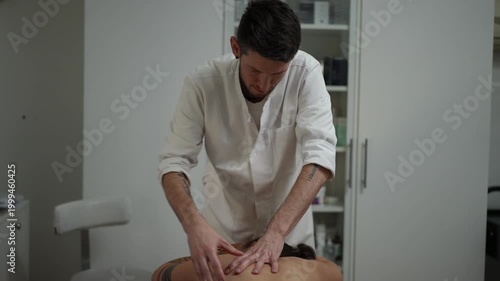 Male therapist applying pressure on a client's back during a massage session. A masseur at work focusing on relieving muscle tension