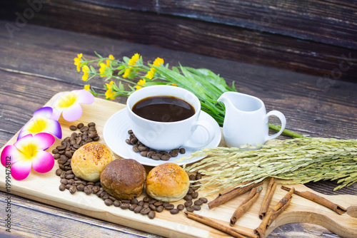 Still life coffee scene with cup of black coffee, bread, coffee beans, sunflower and cinnamon on wooden background, warm cozy cafe