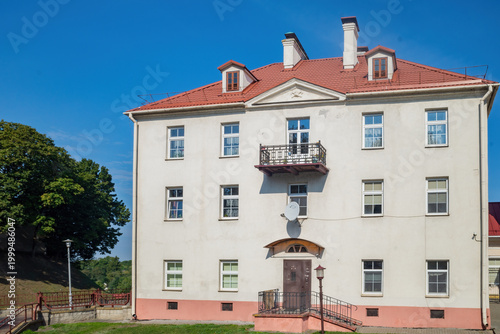 Classic three story apartment building with a red roof and small balconies under a blue sky
