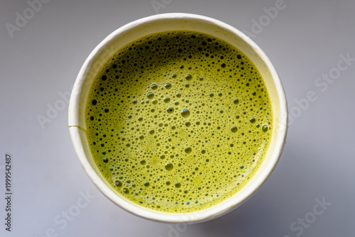 Close Up of Paper Glass Hot Matcha or Green Tea take-away, Top Angle View. Wooden table and place for Text and Graphic Resources.