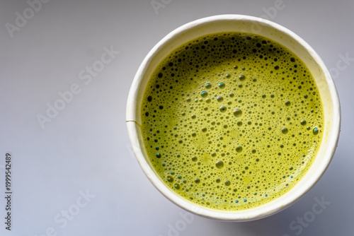 Close Up of Paper Glass Hot Matcha or Green Tea take-away, Top Angle View. Wooden table and place for Text and Graphic Resources.