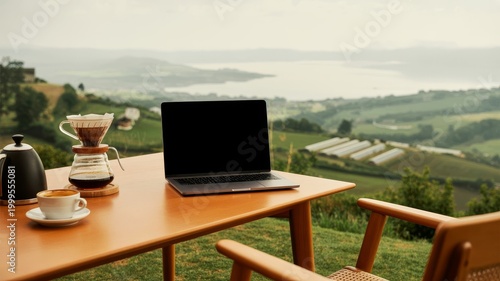 A serene outdoor workspace featuring a laptop, coffee, and brewing equipment, overlooking a beautiful landscape.
