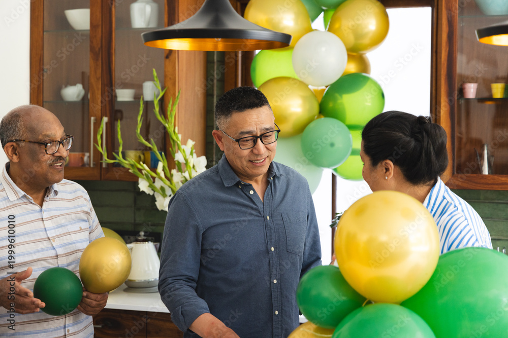 Naklejka premium Diverse family with senior men and woman decorating with green and gold balloons in kitchen