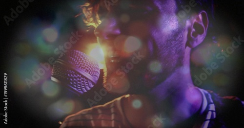 Male singer in striped shirt singing into handheld mic at concert, with backlight haze bokeh