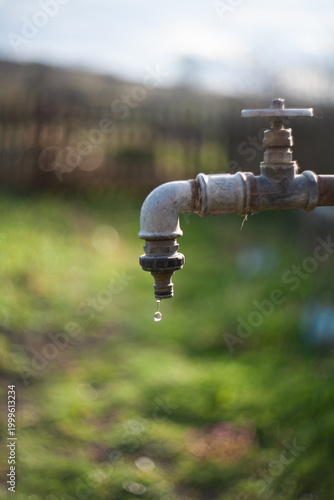 Rustic faucet dripping water outdoors representing conservation drought