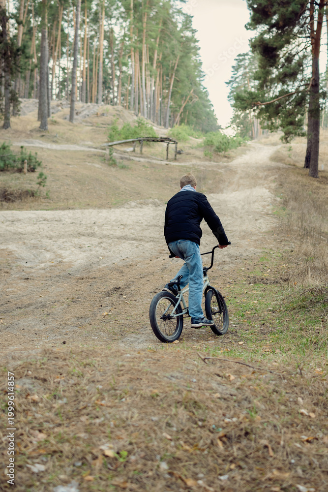 Obraz premium Teenager Riding BMX Bicycle on Sandy Trail in Pine Forest Outdoor Adventure and Active Lifestyle