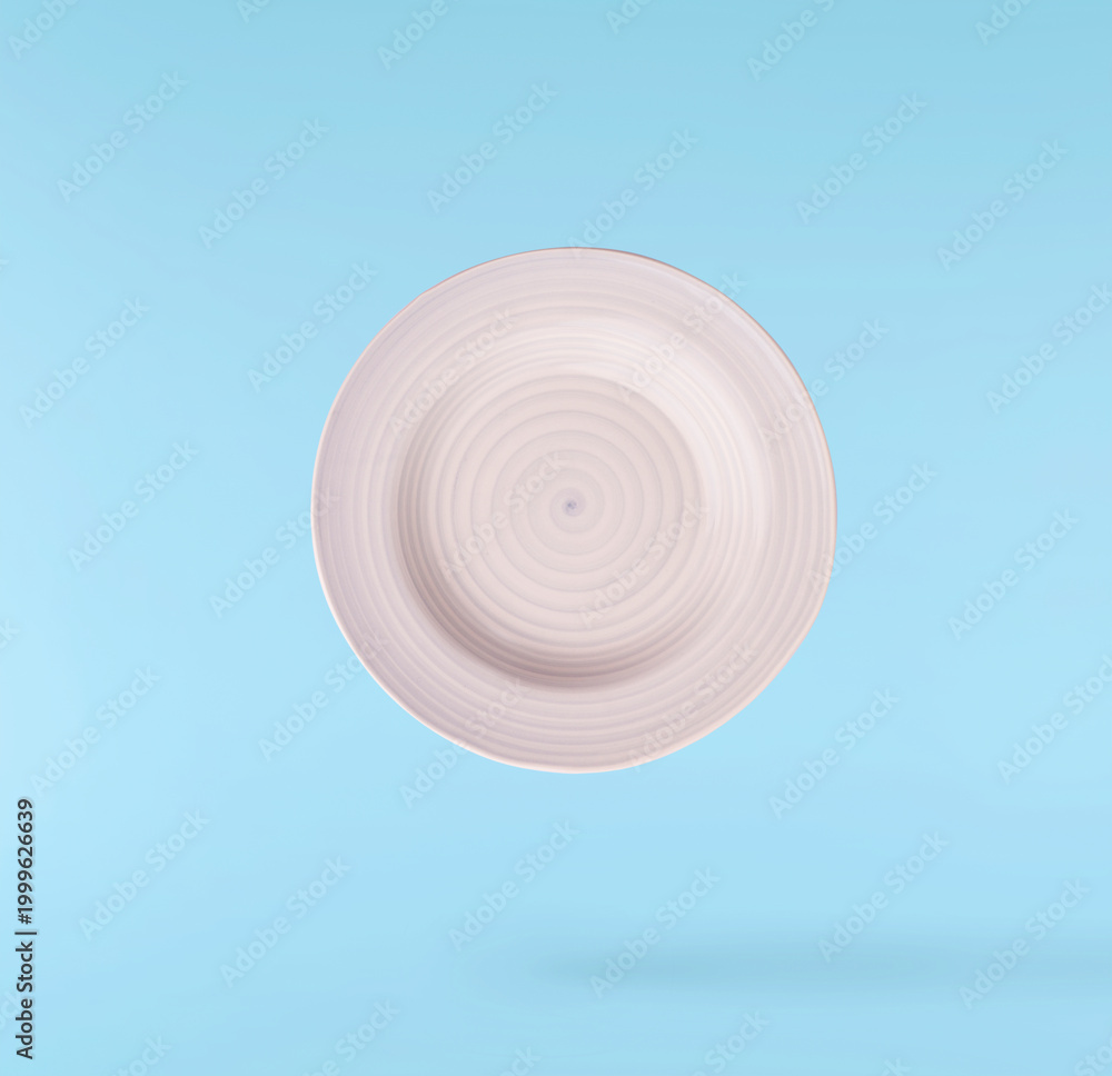 Obraz premium Levitating empty ceramic plate isolated on a pastel blue background. Minimalist zero gravity studio tableware photography concept.