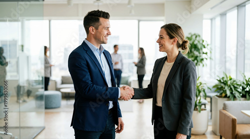 Smiling business people shaking hands in modern office. Professional man and woman concluding successful meeting or greeting client