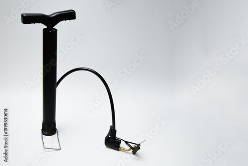 A black pump hand pump with multiple attachments and a leg handle lies on the side on a white background with space for text. High quality photo