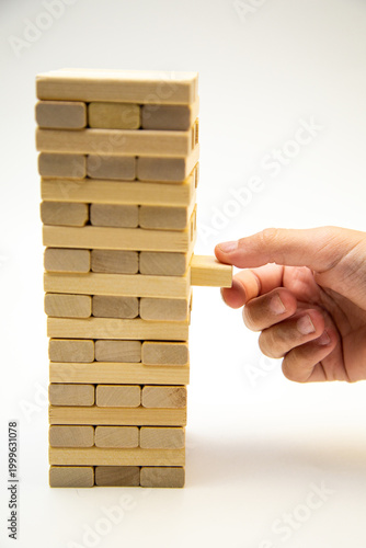 A tower made of wooden bars, a game of gengo, stands on a white background, on the side the hand takes out a wooden block starting the game. The concept of board games, business, construction. High