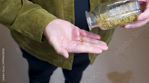 Person pouring dried herbs from a glass jar into their palm, showcasing the process of ingredient preparation in a brewery setting