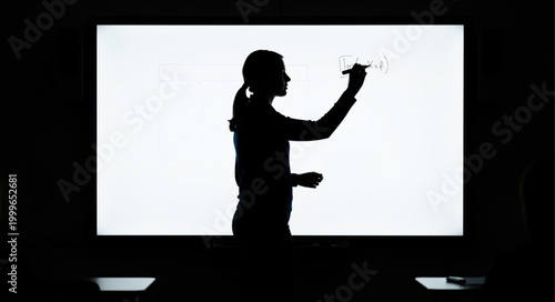 Silhouette of a woman writing on a bright screen in a dark room.