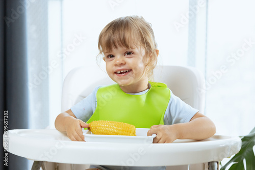 A cute little child girl eating boiled corn cob, a healthy snack for a toddler. Vegetarian meal for a child