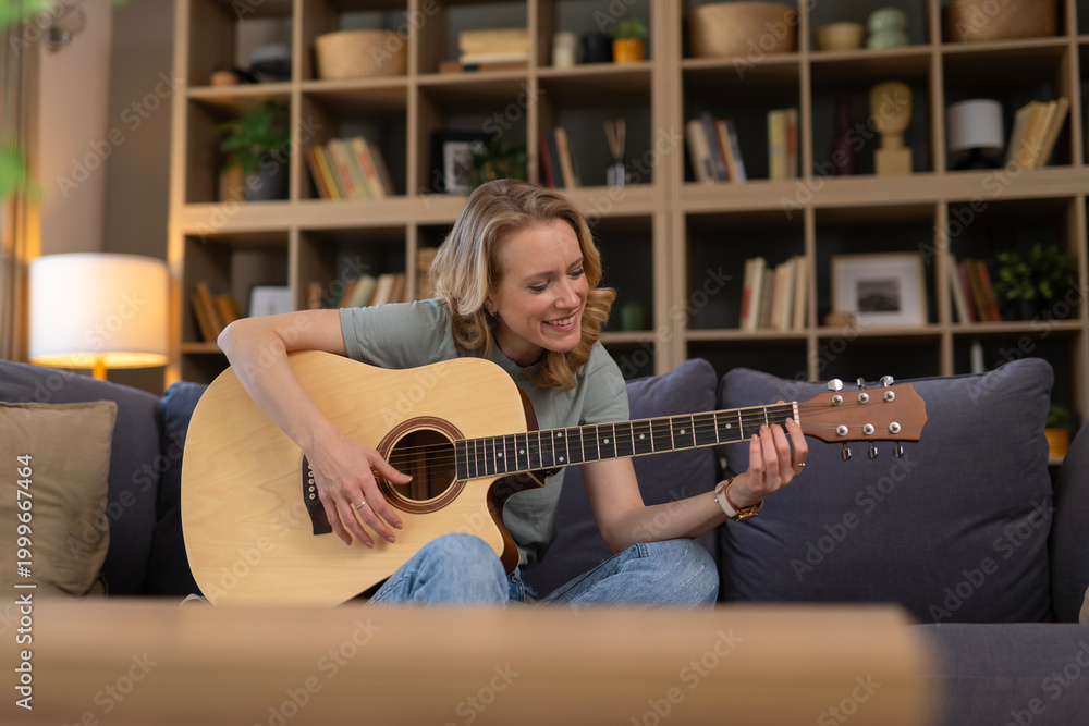 Obraz premium Woman playing acoustic guitar on sofa at home