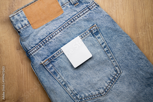 Foto Denim jeans with a blank price tag placed in the back pocket, displayed on a wooden surface, showcasing the fabric texture and stitching details