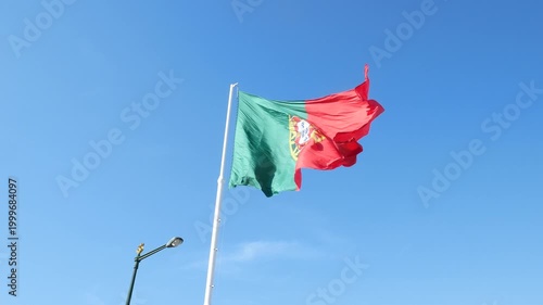 Largest Portuguese flag waving in strong wind in Lisbon on April 25, Carnation Revolution Day, against a clear blue sky, symbolizing freedom, democracy, and national pride.