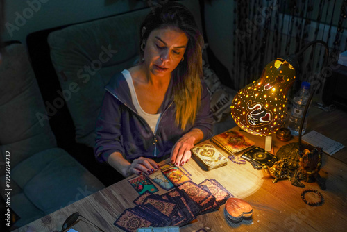 Canvas-taulu Woman fortune teller reading tarot cards with mystical gourd lamp at night