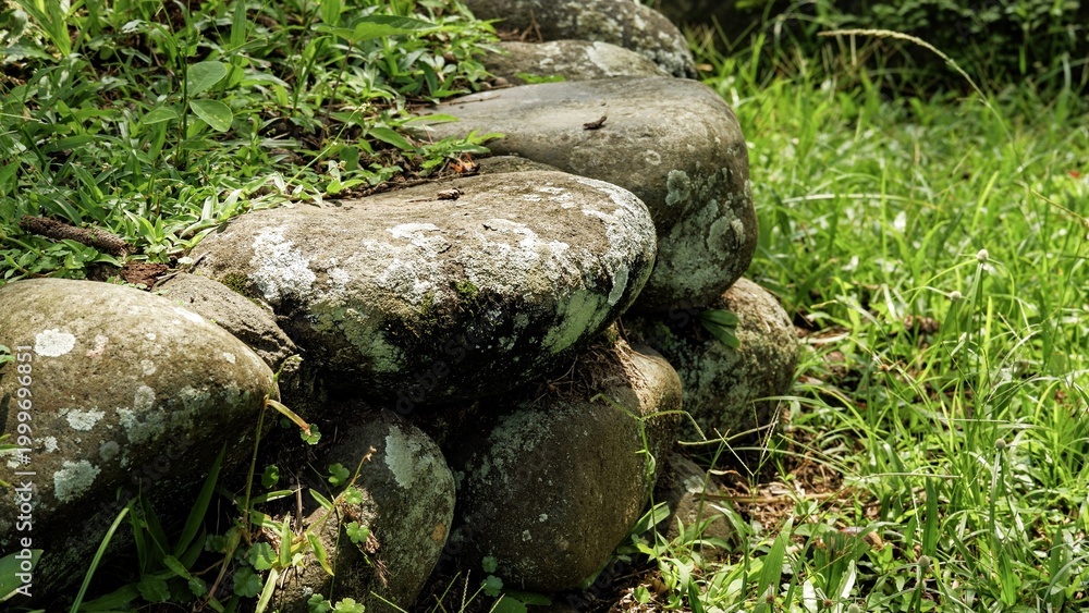 Obraz premium High-angle view of a contemporary stone formation in a lush garden. This architectural landscape feature showcases rugged masonry, organic textures, and various mineral shapes for modern design.