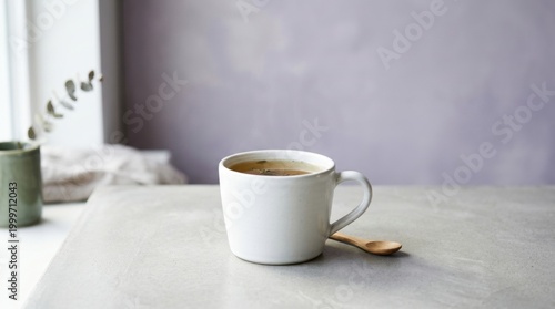 Minimal white coffee cup with golden spoon on neutral tabletop for cozy breakfast background and banner design