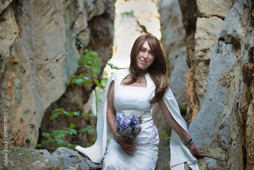 Elegant Woman in White Dress with Lavender Bouquet Posing in Natural Stone Canyon