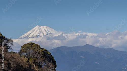Iconic snow-capped Mount Fuji peeks through clouds above misty Japanese mountains