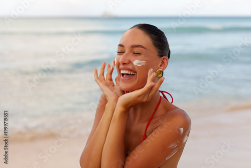 Foto Closeup of smiling young woman applying sunscreen on face at tropical beach