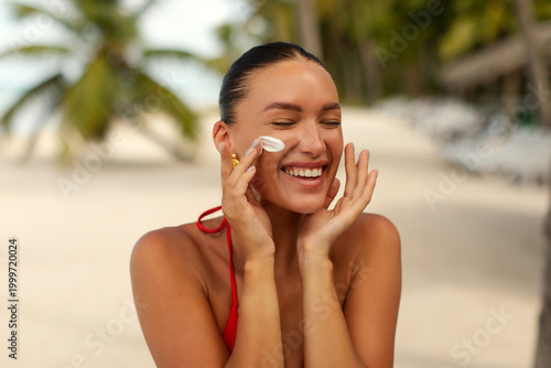 Принти на полотні Smiling woman applying sunscreen cream on face while relaxing on tropical beach