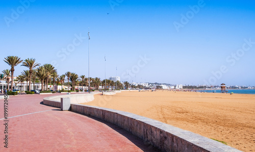 Seafront promenade or Corniche and city beach with palm trees in Agadir, Morocco. Popular tourist area with shops and restaurants. Moroccan seaside resort