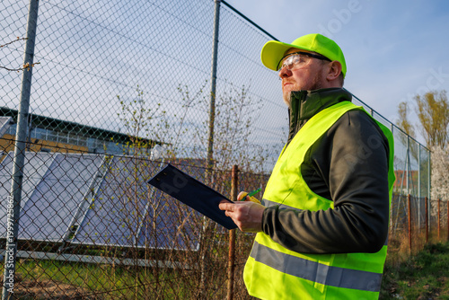 Green energy. Technician worker in a reflective vest works near an area with ground-mounted solar panels. Ecologist inspector monitors the operation of a power plant. 