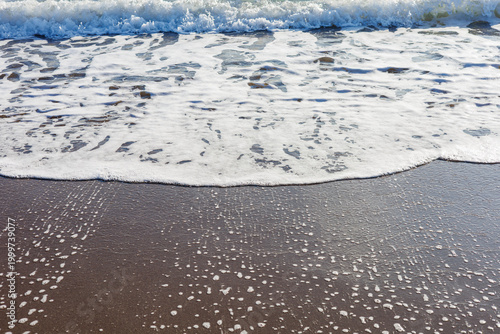 Foamy wave rolling onto dark sandy shore