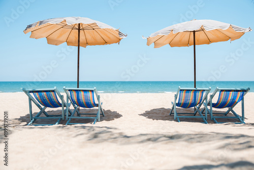 Two colorful beach chairs and striped umbrellas on sunny tropical beach