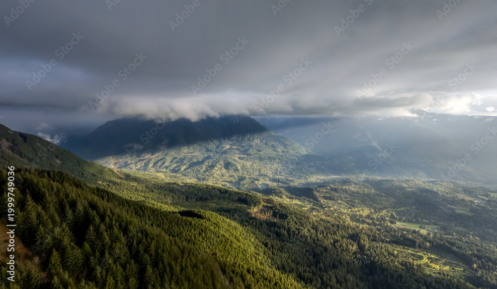 Fototapeta premium Dramatic Cloudscape Over Forested Mountain Valley in British Columbia, Canada With Sunlit Ridges