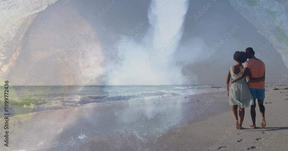 Fototapeta premium Walking couple strolling on wet sand by sea, in sundress shirt, passing waterfall mist, copy space