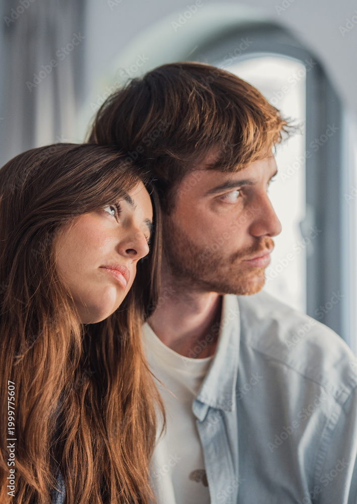 Obraz premium Pensive young couple leaning together in a quiet intimate moment at home, thoughtful and emotional portrait