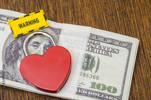 Warning Sign on Red Heart Shaped Padlock Locking Stack of Cash for Financial Safety and Relationship Scam Warning Concept